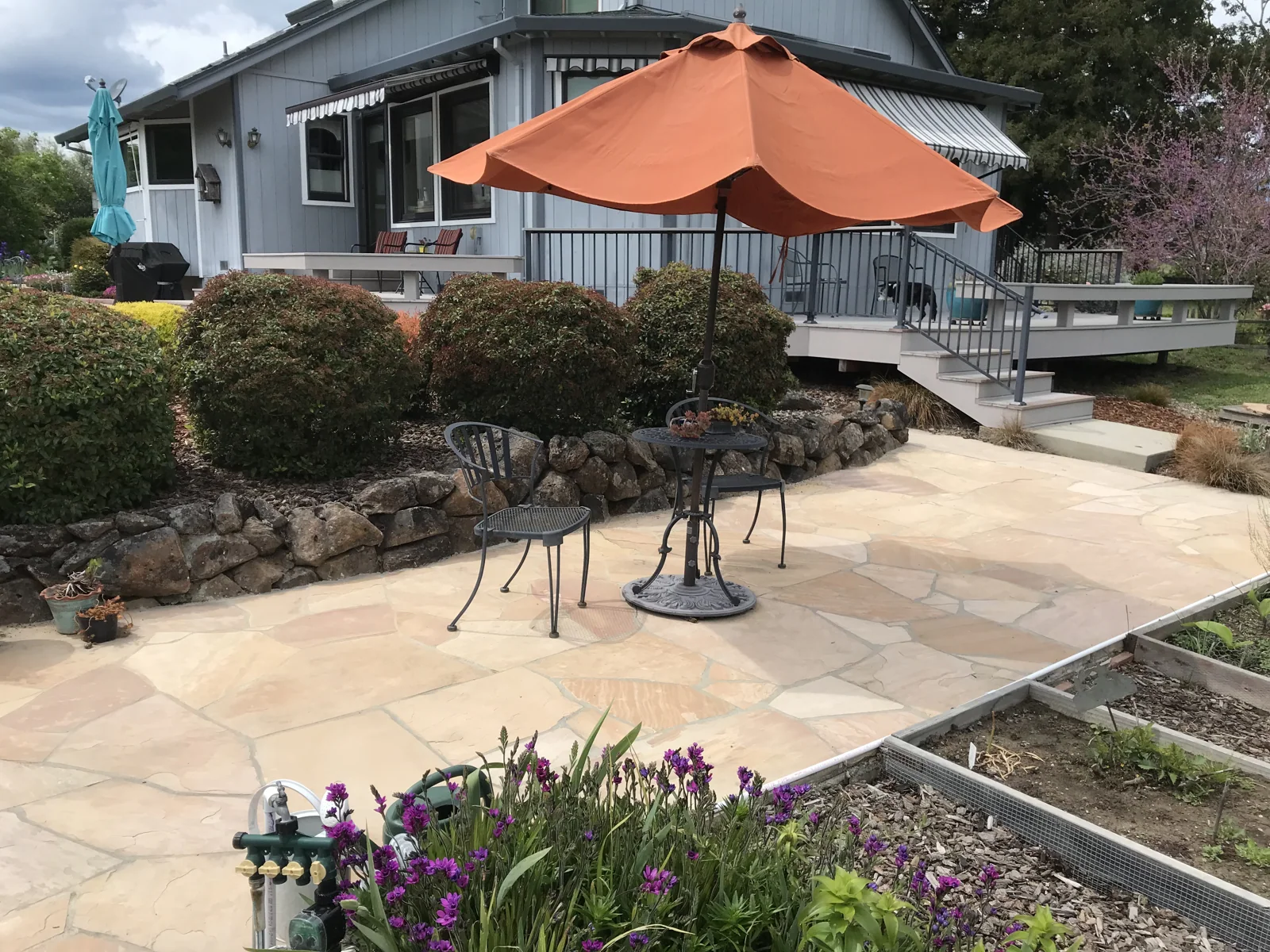 A fitted stone patio beside a garden, with an orange umbrella and outdoor seating