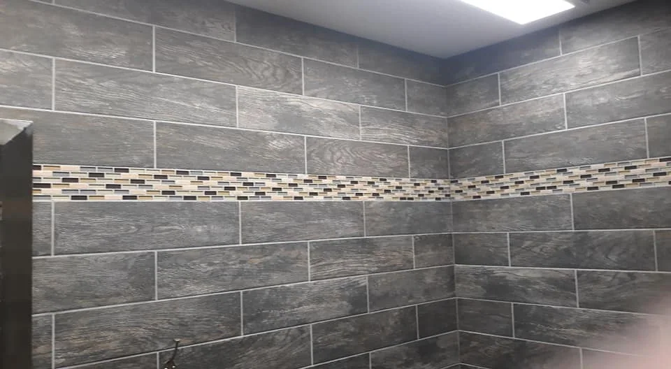 Grey bathroom tilework with a horizontal mosaic border from Award Winning Masonry’s portfolio