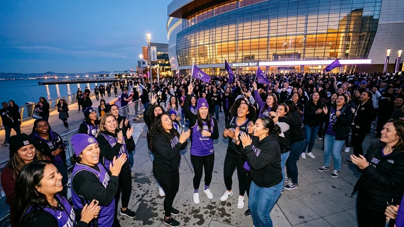 Women’s basketball fans in violet and black attire gathered at an outdoor waterfront arena plaza in San Francisco at dusk