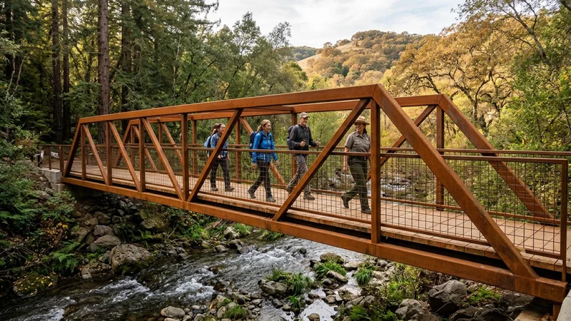 Hikers and park rangers crossing a 65-foot weathering-steel pedestrian footbridge over a clear rocky stream lined with ferns and redwoods at Lafayette Community Park in Lafayette