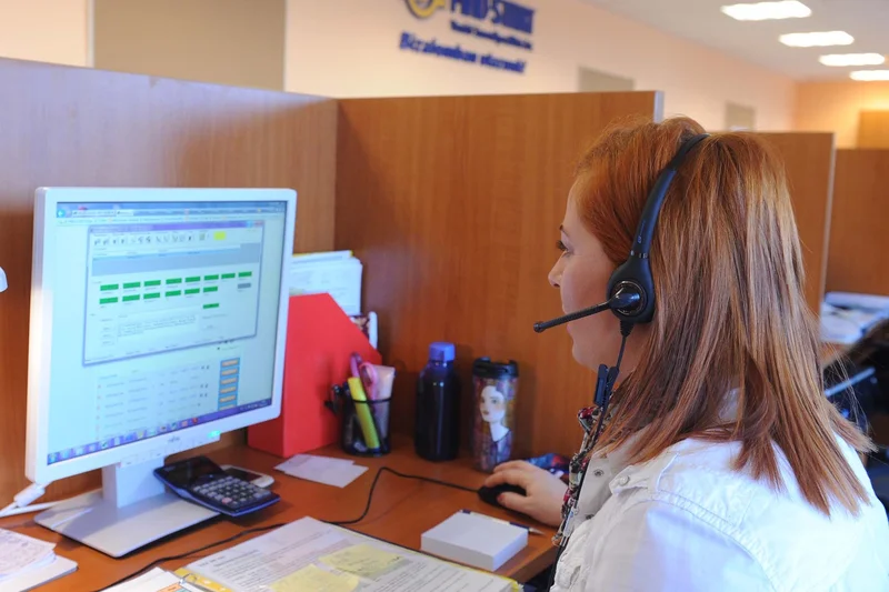Customer service representative wearing a headset at a computer workstation displaying support records